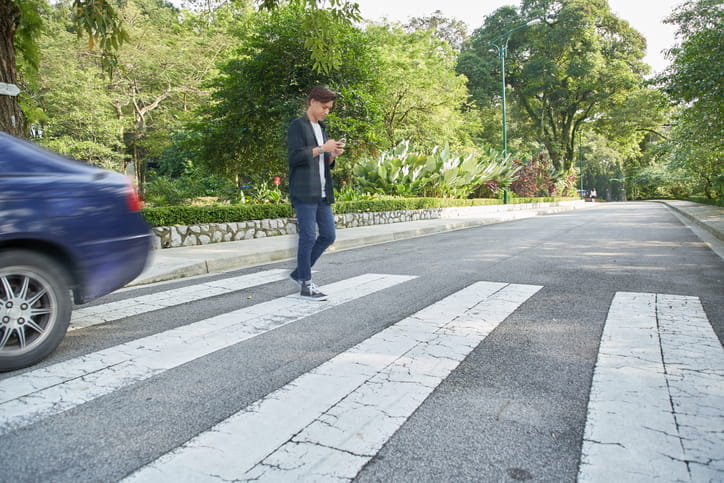 A distracted pedestrian crossing a crosswalk while texting on his phone.