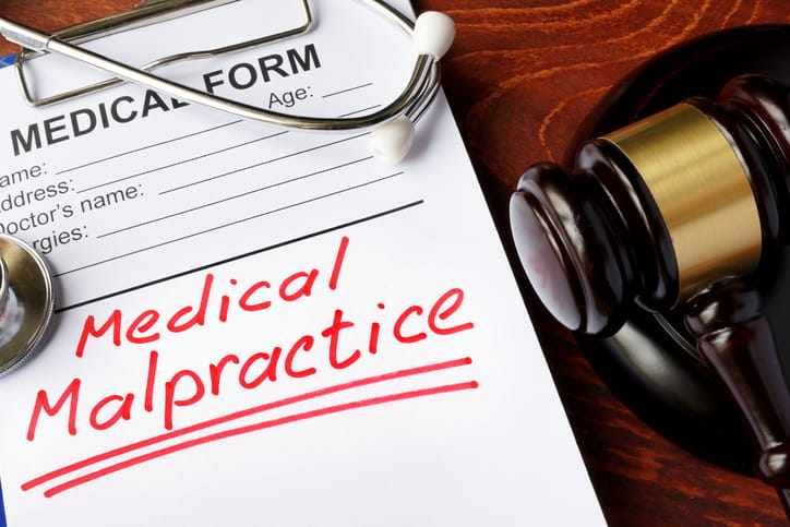 A medical form that has "Medical Malpractice" written on it. On top is a stethoscope and both are next to a gavel.